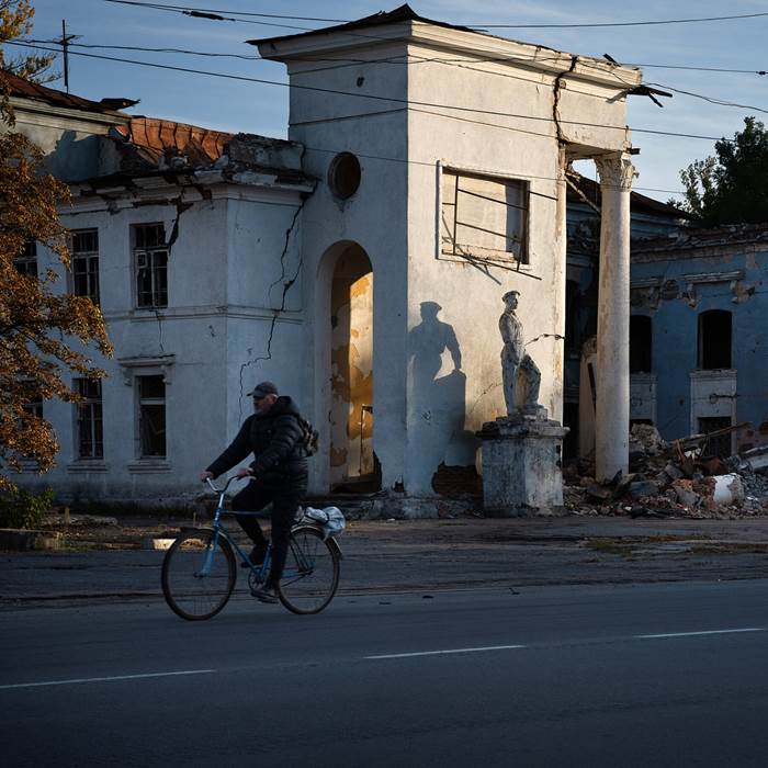 A cyclist passing rubble and damaged buildings.